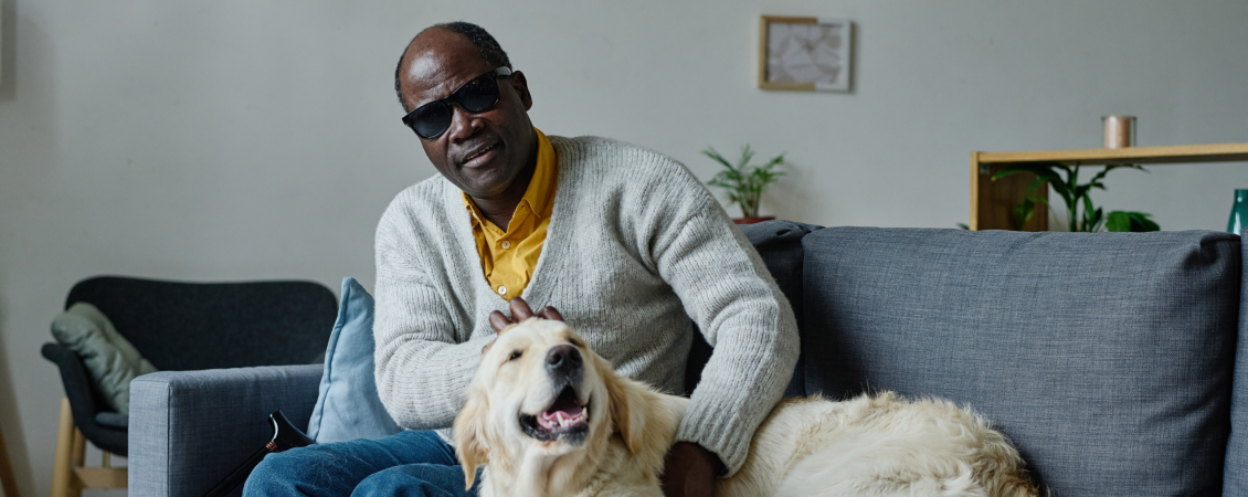 Man wearing dark shades sitting on couch with a golden retriever.