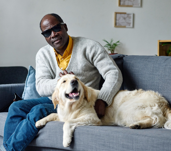 Man wearing dark shades sitting on couch with a golden retriever.