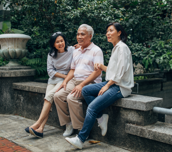 Older man sitting between two women in a park.