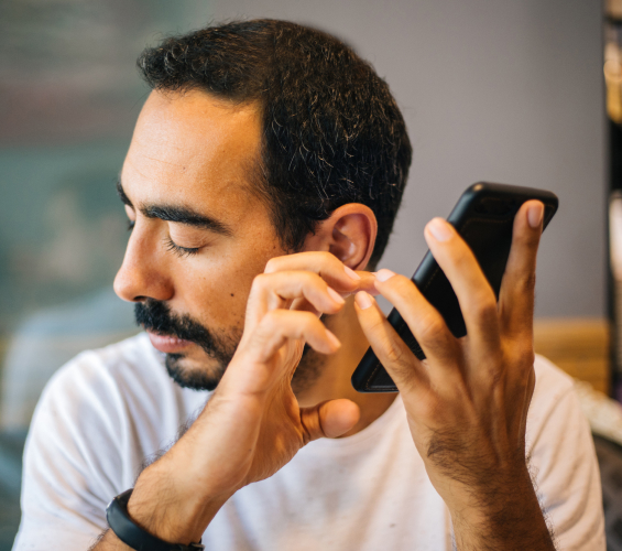 A man holds a smartphone up to his ear while interacting with it.