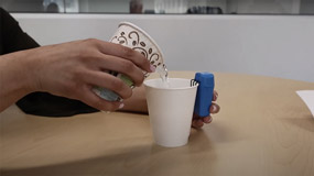 A person pours liquid into a cup attached to a liquid leveler device.