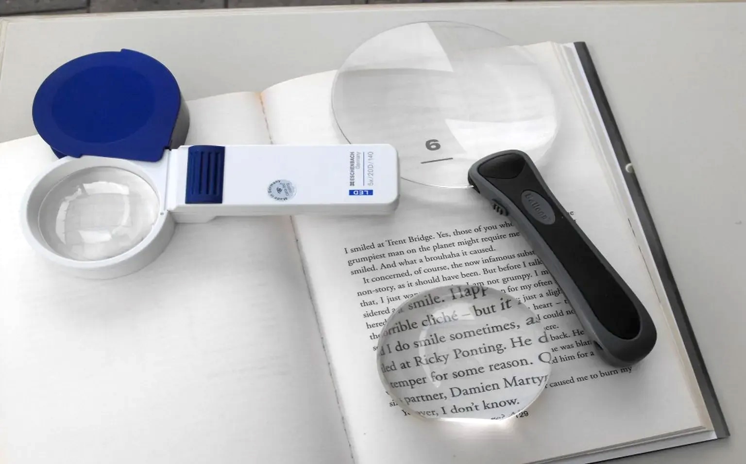 Three magnifying glasses are placed on an open book, with their lenses enlarging portions of the printed text.