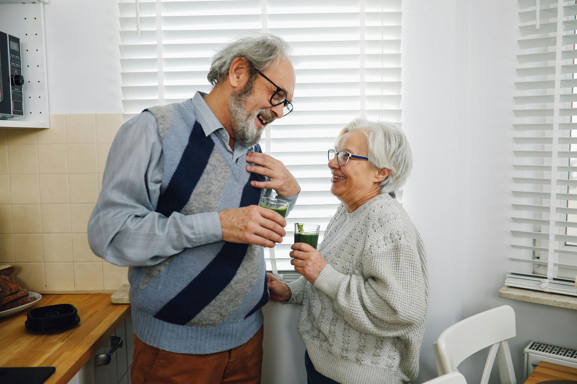 A happy, mature couple enjoying smoothies in their kitchen.