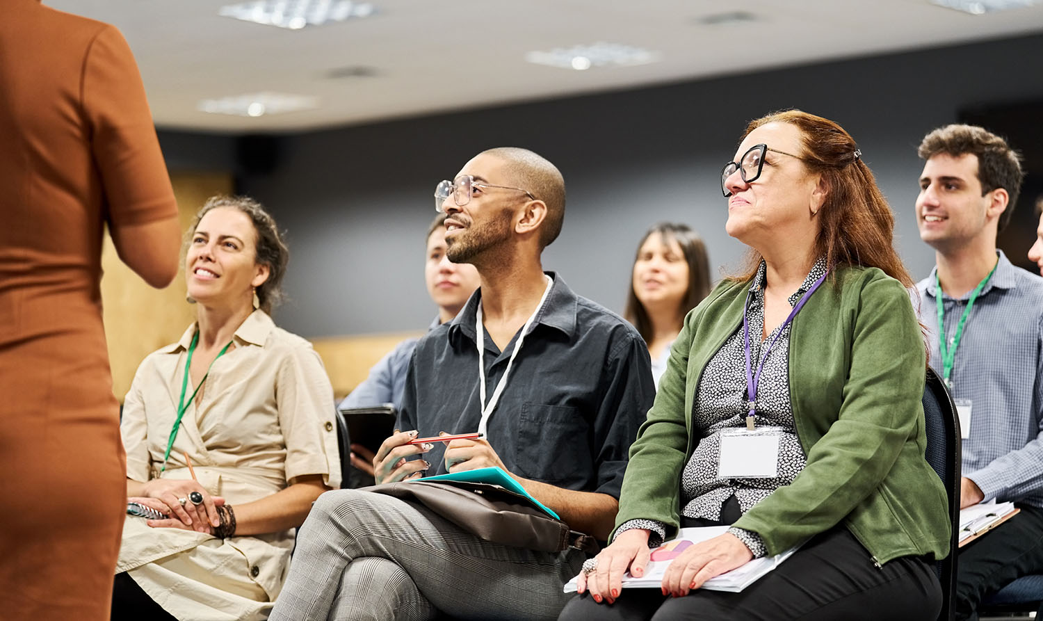 A diverse group of professionals in a meeting room,, actively engaged in listening to a speaker who is presenting information.
