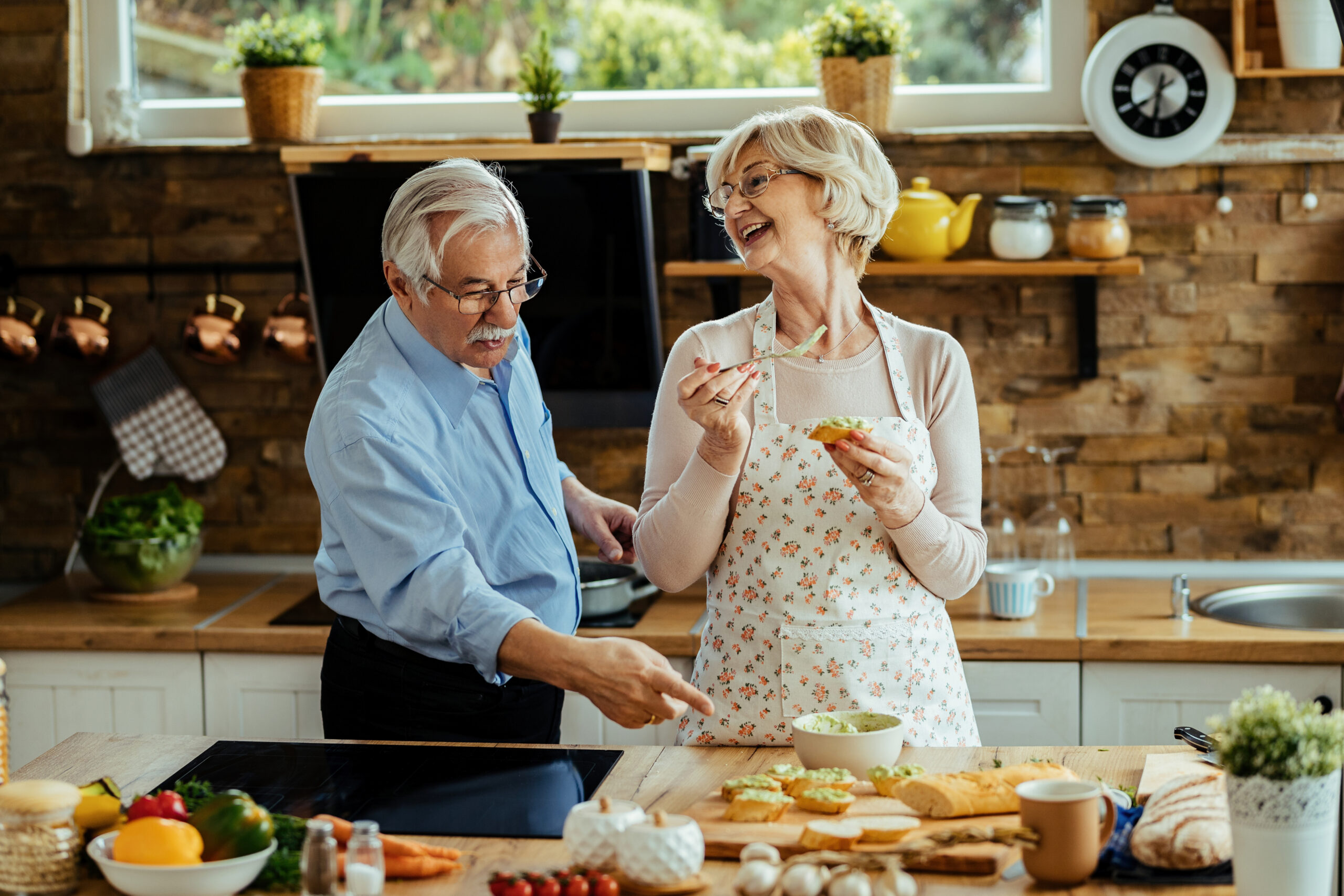 A happy, mature couple talking and having fun while preparing food in their kitchen.
