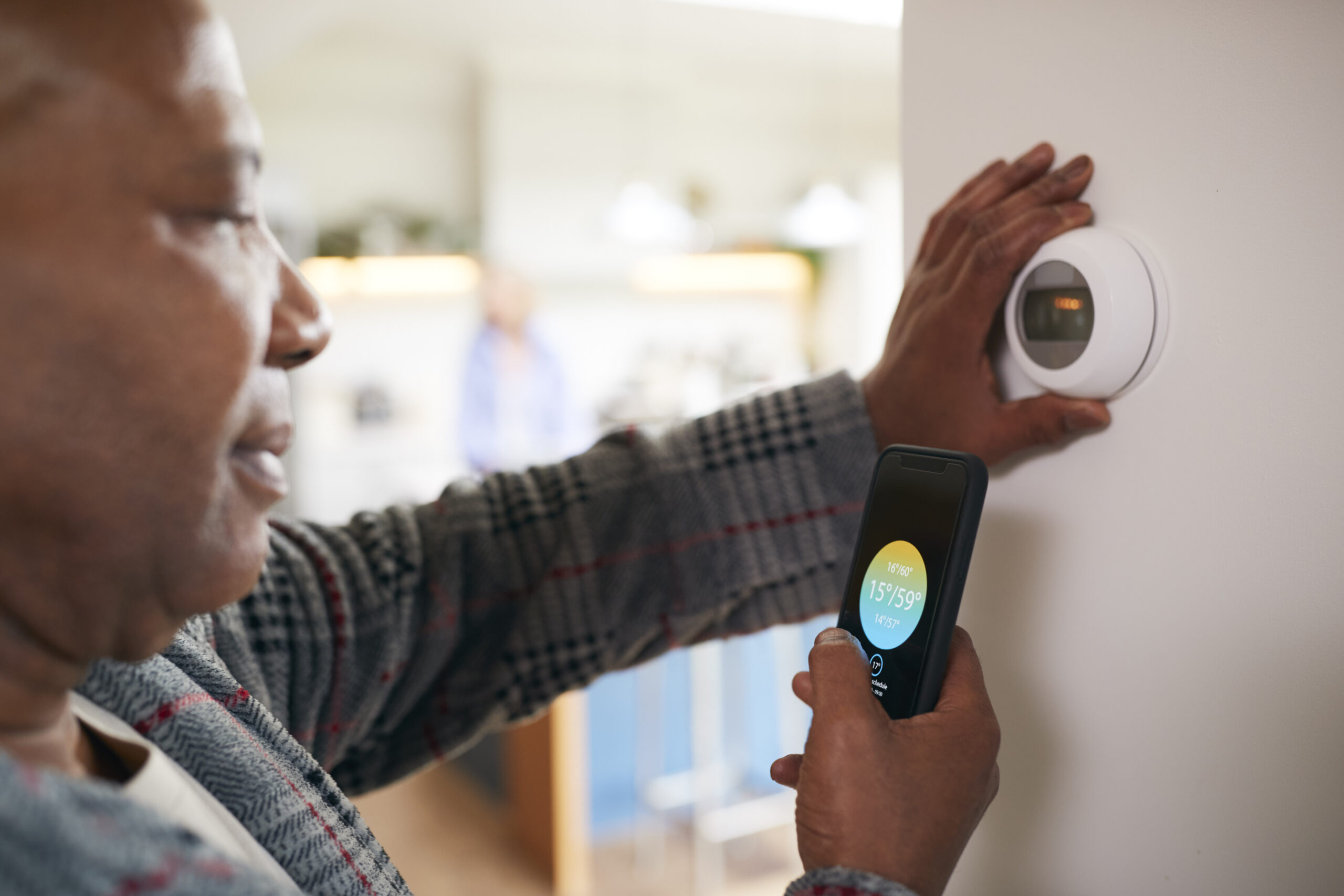 A person adjusts a smart thermostat using a smartphone app.