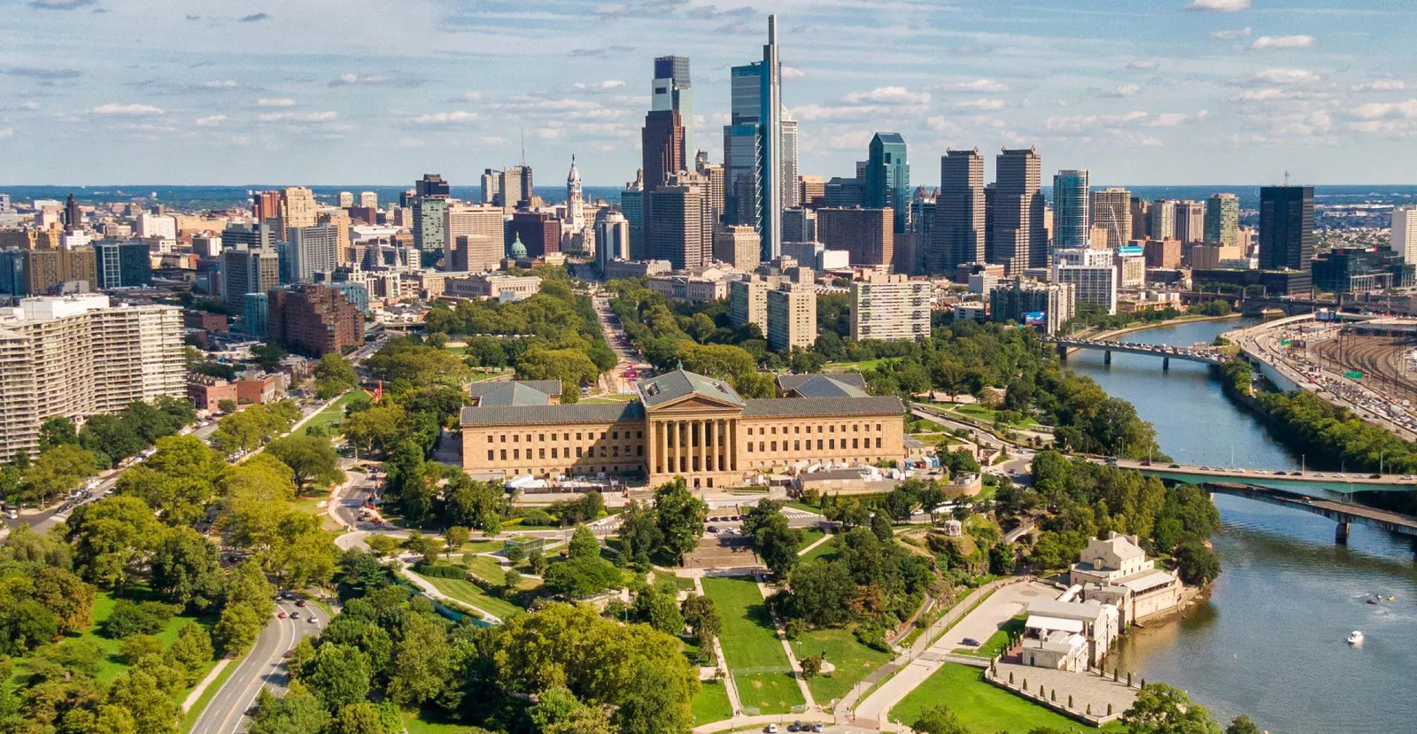 Aerial view of Philadelphia in the summer, with Philadelphia Museum of Art and the Schuylkill River in the foreground, and the city skyline in the background.