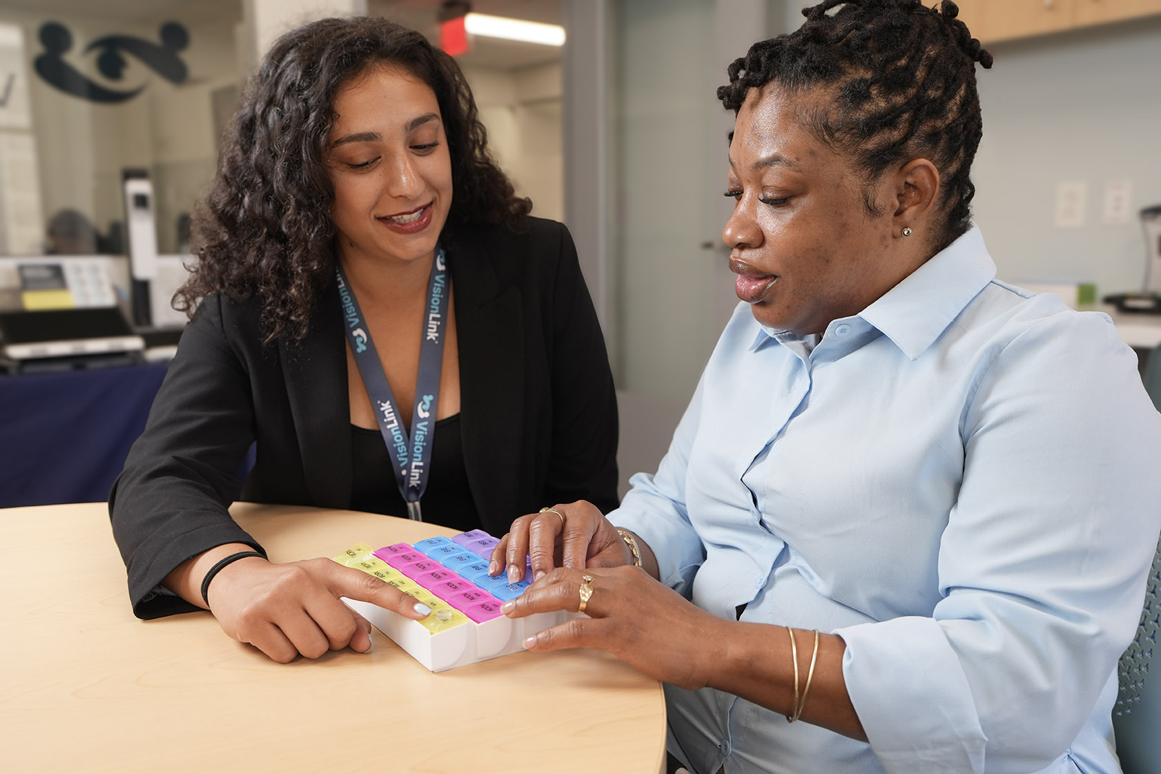 VisionLink vision rehabilitation therapist Sofiya assists a client with a pill sorter at a round table.